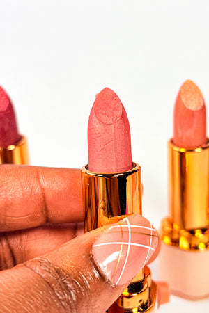Close-up of a hand holding a pink lipstick with a gold cap against a white background. Bare Blossom Lipstick