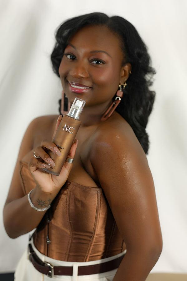 Woman holding a bottle of Naaby Cosmetics shimmer body oil  skin care product against a white background