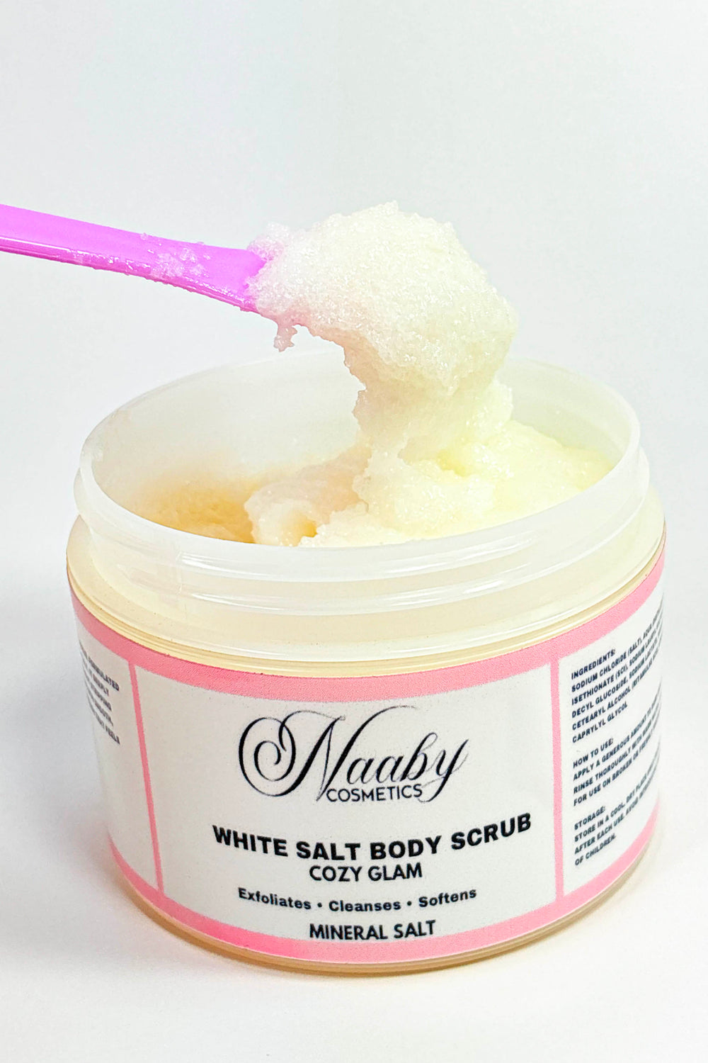 Jar of white salt body scrub with pink label on a white background.Cozy Glam – White  Salt Body Scrub