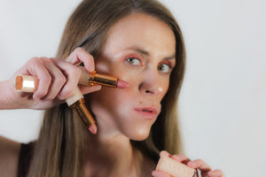 Woman applying makeup with a brush and compact on a plain background