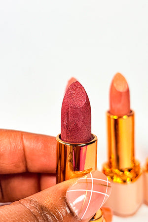 Two lipsticks held by a hand against a white background