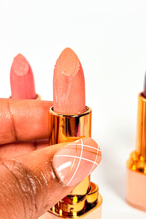 Close-up of a hand holding a pink lipstick with a gold case on a white background