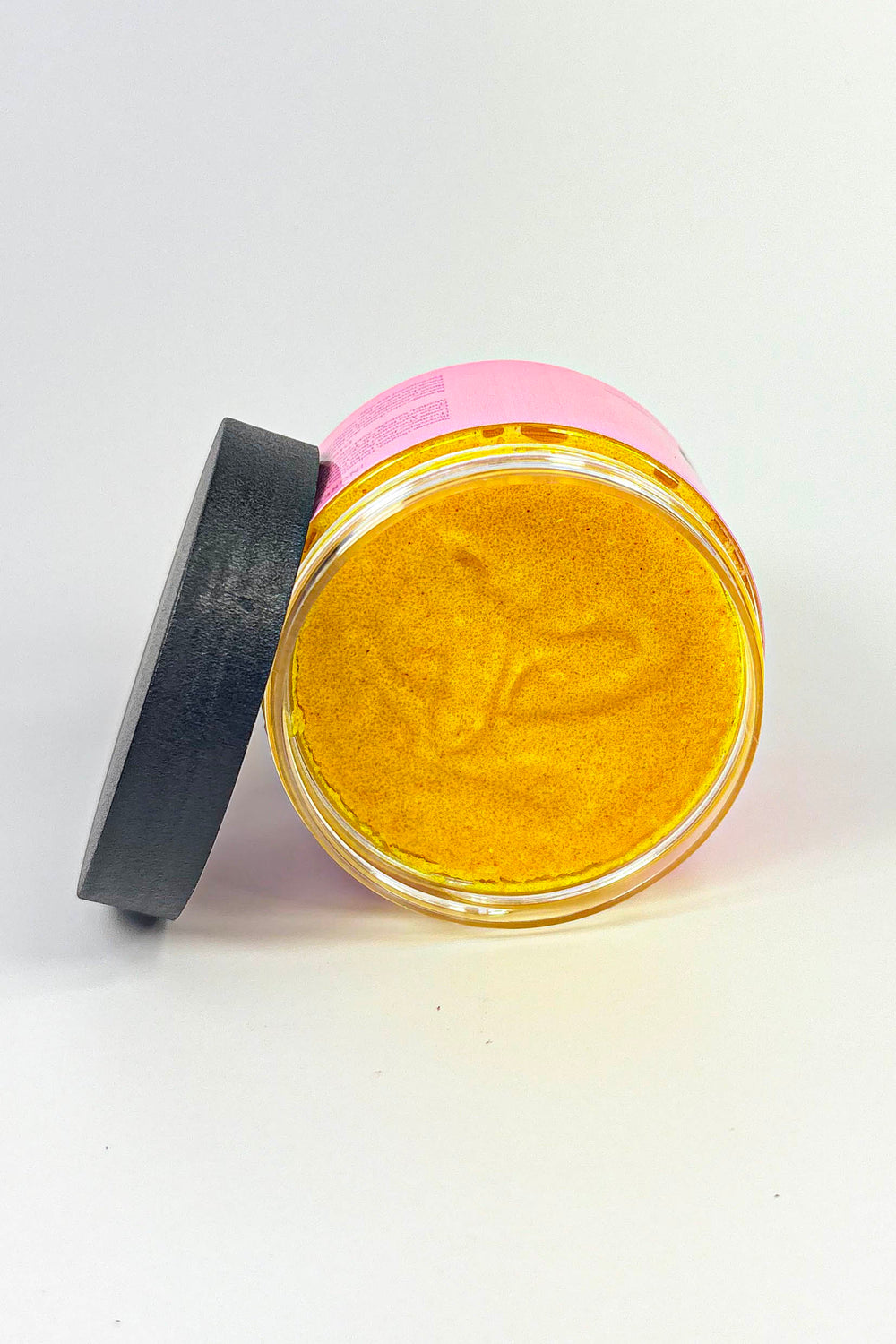Pink facial scrub jar with black lid on a white background-Turmeric Glow Scrub – Brightening Turmeric Sugar Scrub for Dark Spots