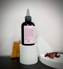 Black bottle with a pink label on a white cylindrical stand against a gray background