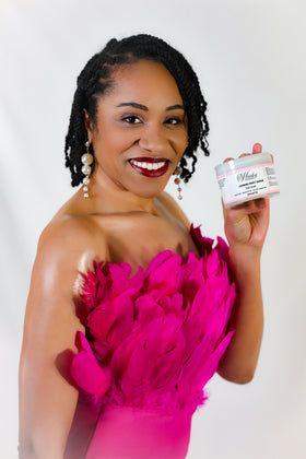 Woman in a bright pink dress holding a jar of Cozy Glam – Foaming Sugar Body Scrub  against a white background