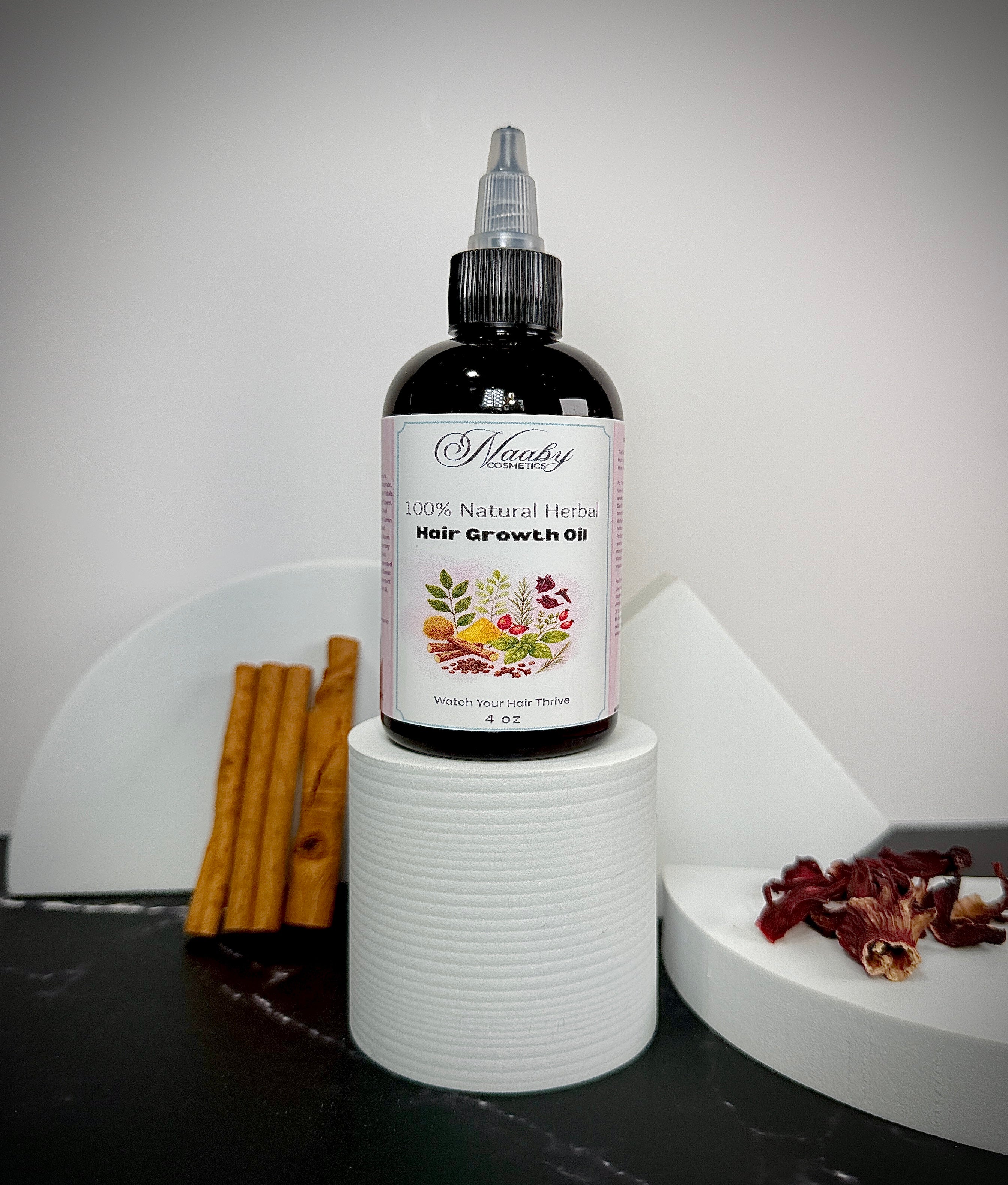 Bottle of natural herbal hair growth oil with cinnamon sticks and dried herbs on a white surface.